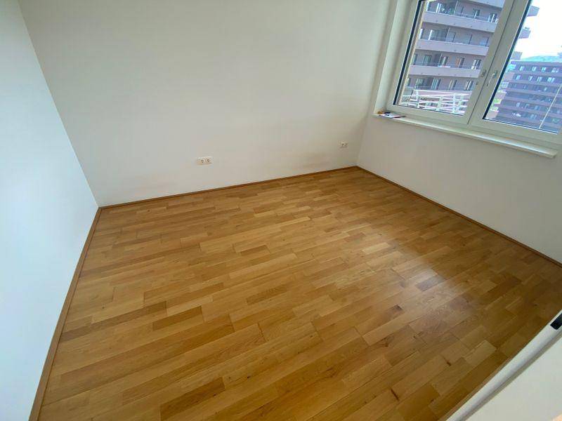 Helles Schlafzimmer mit Holzboden und großem Fenster, das viel Tageslicht hereinlässt.