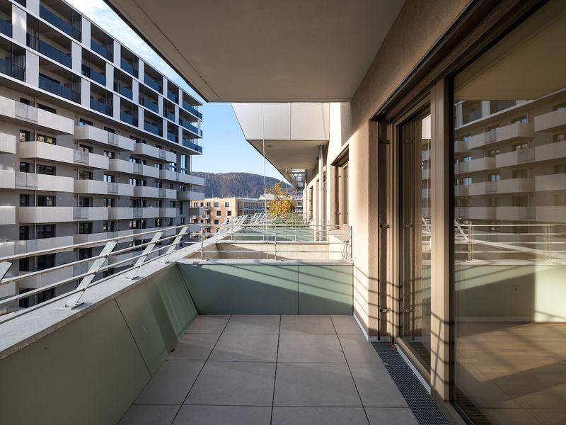 Geräumiger Balkon mit Fliesenboden und Blick auf die umliegenden Gebäude und Berge.