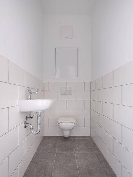 Modernes Gäste-WC mit weißen Wandfliesen, Hänge-WC und kleinem Waschbecken.