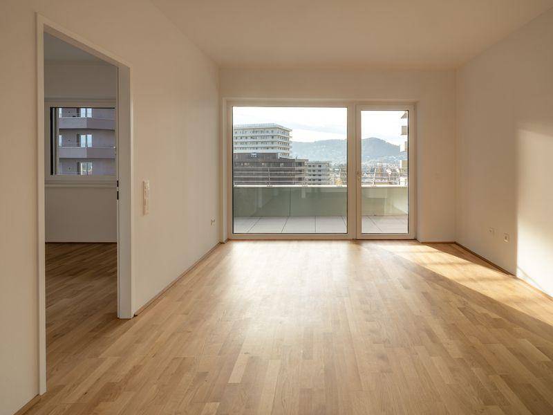 Helles Wohnzimmer mit Parkettboden, großen Fenstern und Zugang zu einem Balkon mit Stadtblick.