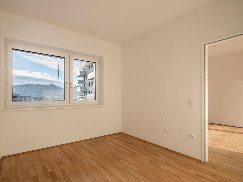 Leeres Schlafzimmer mit Parkettboden und Fenster, das einen weiten Blick bietet.