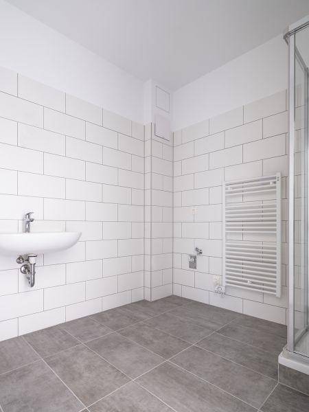 Helles Badezimmer mit weißen Fliesen, Dusche und beheiztem Handtuchhalter.
