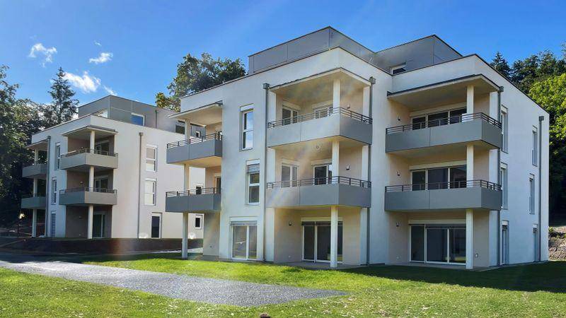 Modernes Mehrfamilienhaus mit mehreren Balkonen und zeitgenössischer Architektur, umgeben von Grünflächen.