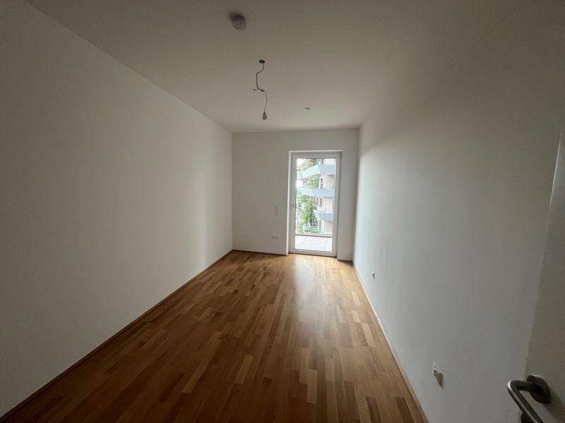 Leerer Raum mit Holzboden und Zugang zu einem französischen Balkon, hell und modern.