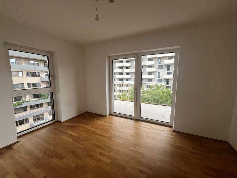 Helles Schlafzimmer mit Holzboden und großen Fenstern, die Zugang zu einem Balkon ermöglichen.
