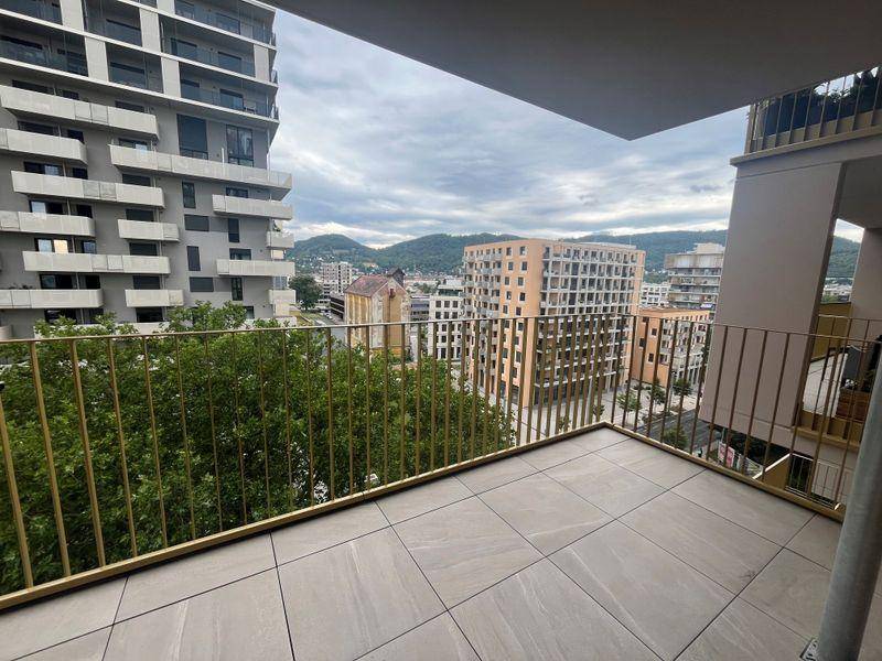 Heller Balkon mit Fliesenboden und Panoramablick auf die Stadt und die grüne Umgebung.