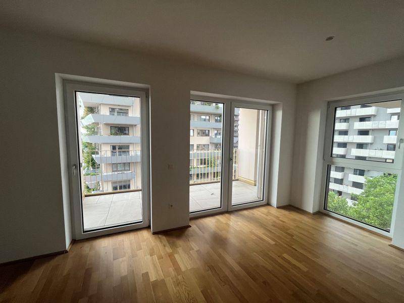 Geräumiger Raum mit Holzboden und großen Fenstern, die Zugang zu einem Balkon bieten.