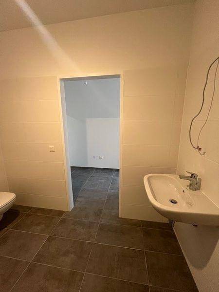 Helles Badezimmer mit modernem Waschbecken und Fliesenboden, Blick in einen weiteren Raum.
