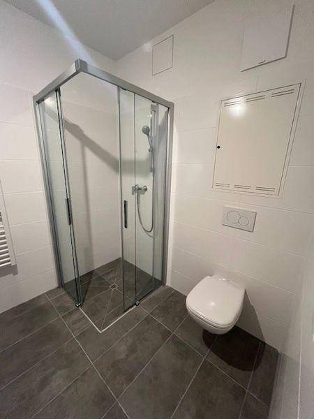 Modernes Badezimmer mit Duschkabine, wandhängendem WC und hellen Fliesen.