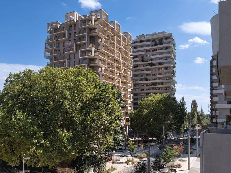 Moderne Wohngebäude mit vielen Balkonen, umgeben von Bäumen und städtischer Infrastruktur.
