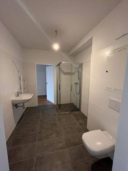 Modernes Badezimmer mit Dusche, Waschbecken und Wand-WC, ausgestattet mit dunklen Bodenfliesen.