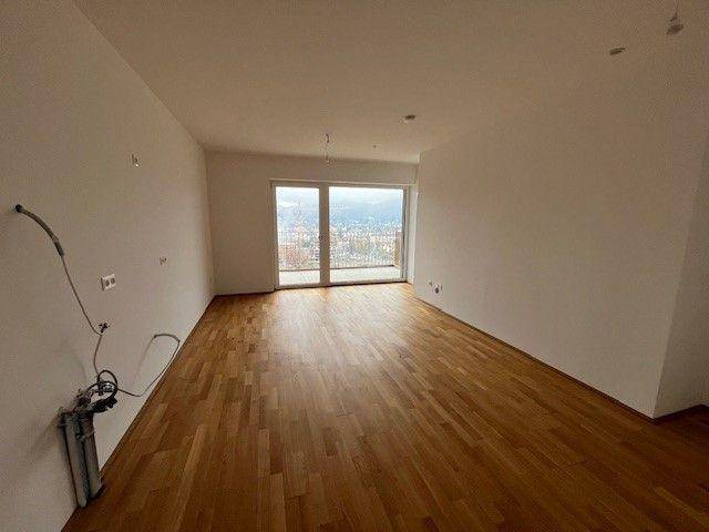 Geräumiges, leeres Wohnzimmer mit hellem Parkettboden und weitem Blick durch große Fenster.