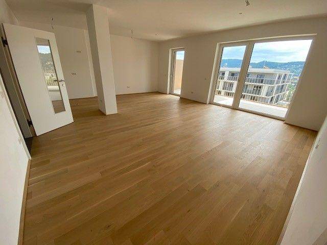 Lichtdurchflutetes Wohnzimmer mit großen Fenstern, Holzplankenboden und Blick auf die Umgebung.