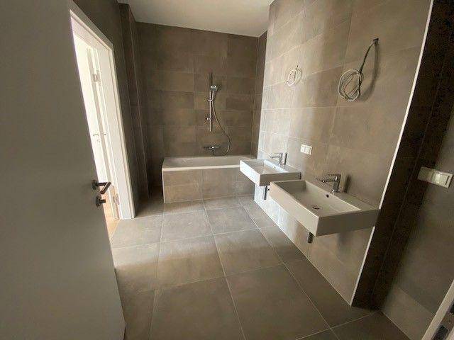 Geräumiges Badezimmer mit zwei Waschbecken, Badewanne und modernen grauen Fliesen.