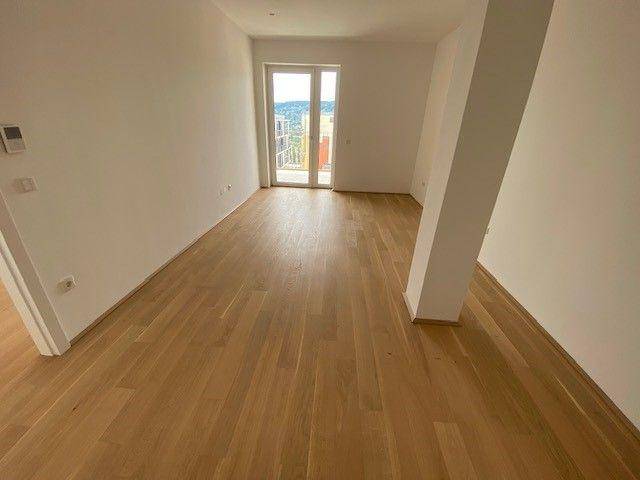 Helles Wohnzimmer mit hellem Holzplankenboden, weißen Wänden und Zugang zu einem Balkon.