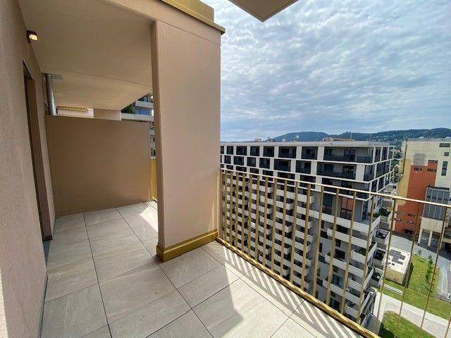 Balkon mit modernem goldenem Geländer und Fliesenboden, mit Blick auf umliegende Gebäude und Landschaft.
