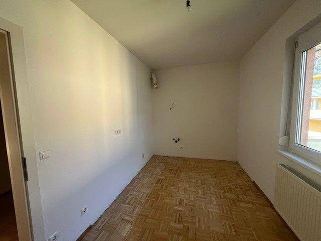 Leeres Schlafzimmer mit Parkettboden und einem Fenster, das Tageslicht hereinlässt.
