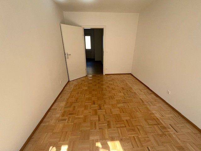 Leeres Zimmer mit Parkettboden und offener Tür zu einem weiteren Raum.