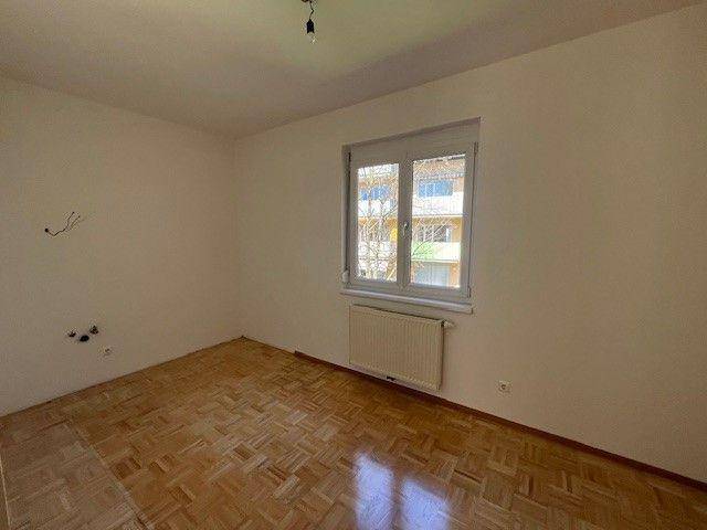 Helles Schlafzimmer mit Parkettboden und Heizkörper unter dem Fenster.