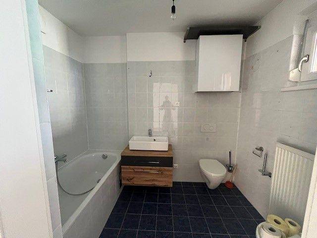 Badezimmer mit Badewanne, Waschbecken, Toilette und dunklen Bodenfliesen.