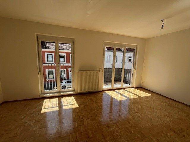 Helles Wohnzimmer mit Parkettboden und zwei großen Fenstern zur Straße.