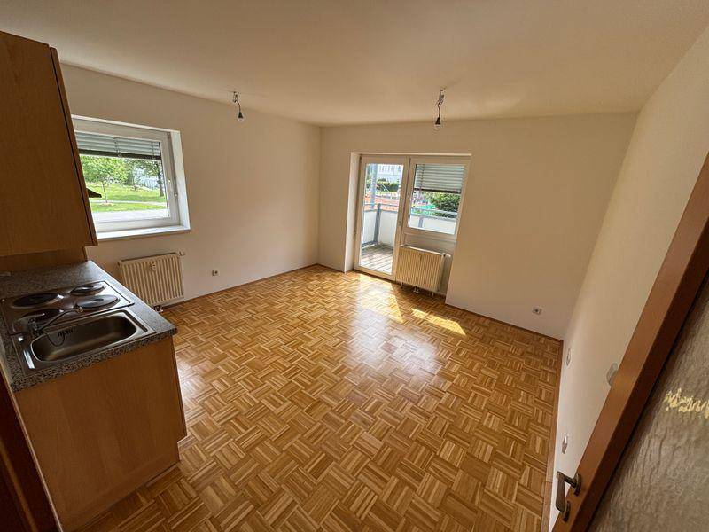 Heller Wohnbereich mit Parkettboden, Zugang zum Balkon und einer kleinen Küchenzeile.