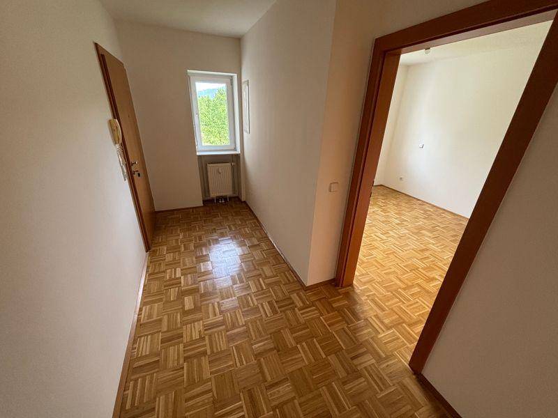 Eingangsbereich mit Parkettboden und einem Fenster, das Tageslicht hereinlässt.