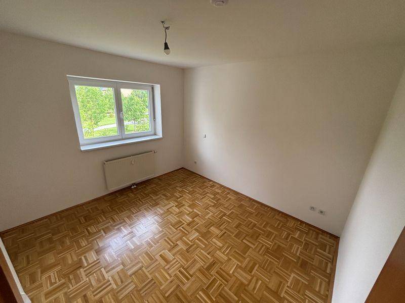 Leeres Schlafzimmer mit Parkettboden und einem großen Fenster mit Blick ins Grüne.