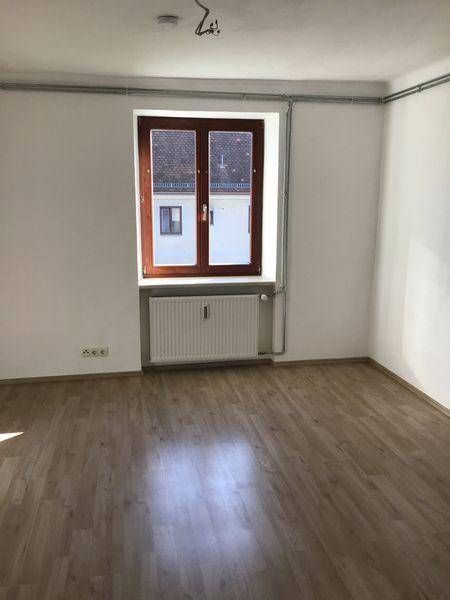 Leerer Raum mit Laminatboden, einem Fenster und Heizkörper, bereit zur individuellen Gestaltung.