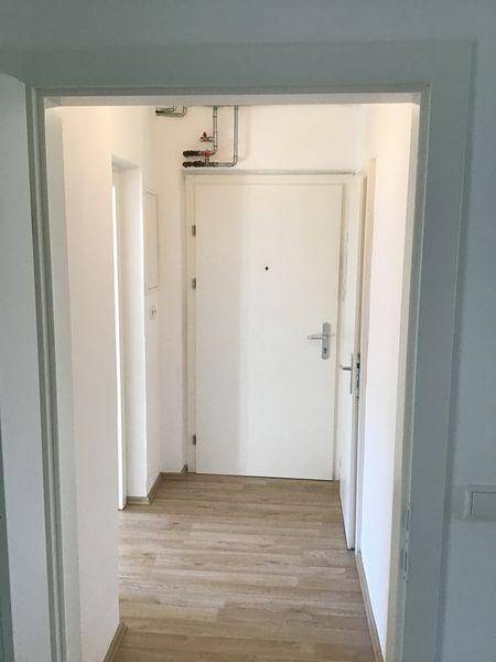 Heller Flur mit Laminatboden und weißer Eingangstür, der in weitere Räume führt.
