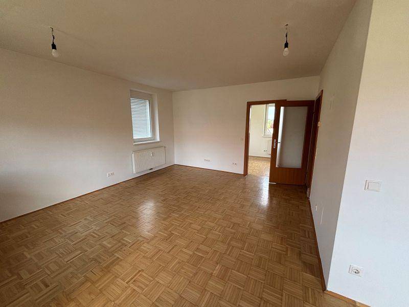 Leeres Wohnzimmer mit klassischem Parkettboden, weißen Wänden und Fenster mit Heizkörper.
