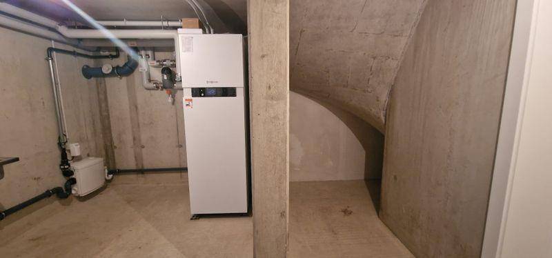 Technikraum im Keller mit Heizungsanlage und sichtbaren Rohren in einem unfertigen Zustand.