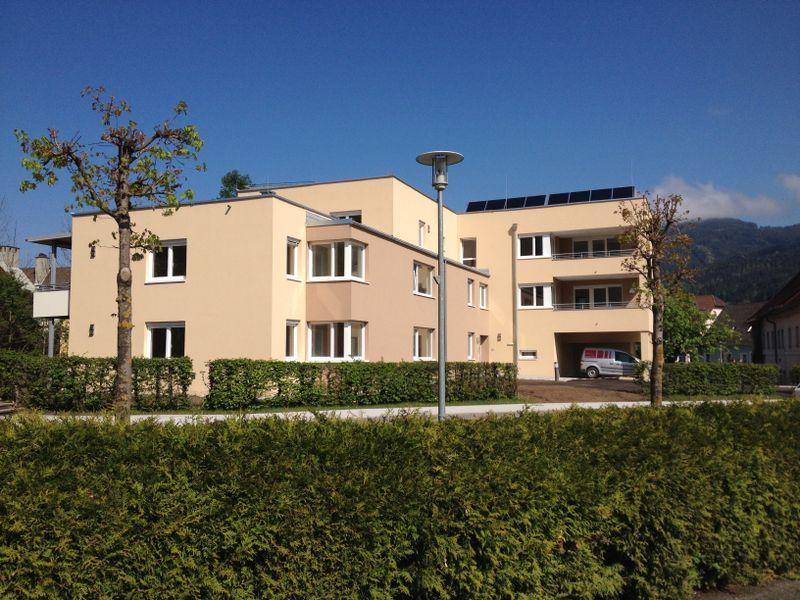 Gesamtansicht eines modernen Wohngebäudes mit Photovoltaikanlage auf dem Dach und grüner Umgebung.
