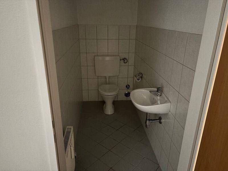 Kleines Gäste-WC mit Toilette, Waschbecken und hellen Fliesen.