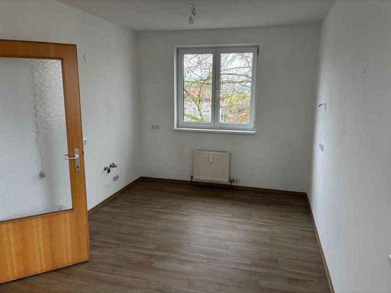 Leerer Raum mit Fenster, Heizkörper und Laminatboden, bereit zur individuellen Gestaltung.