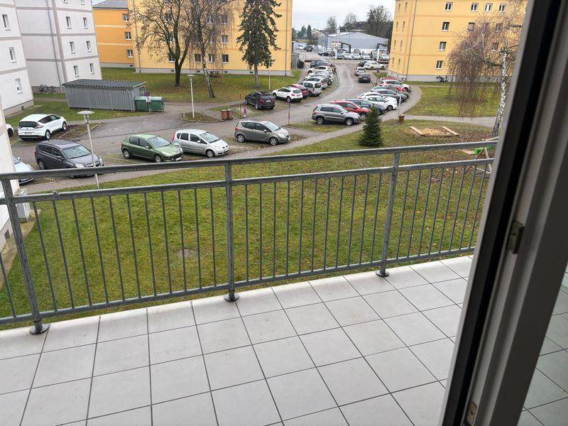 Blick vom Balkon auf den Innenhof mit Parkplätzen und umliegenden Gebäuden.