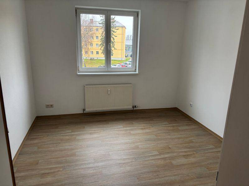 Helles Schlafzimmer mit Laminatboden und Blick auf die umliegenden Gebäude.