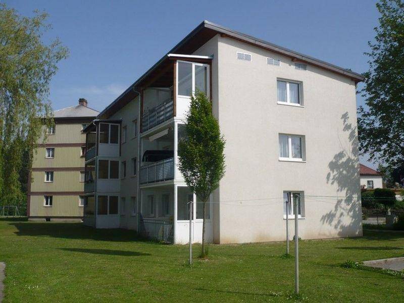 Mehrfamilienhaus mit heller Fassade und Grünfläche im Vordergrund unter blauem Himmel.