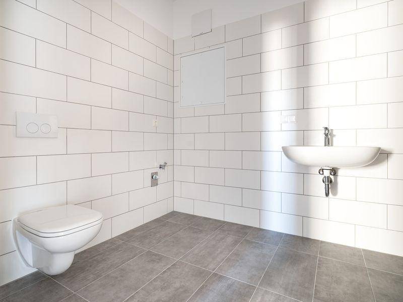 Modernes WC mit weißen Wandfliesen, grauen Bodenfliesen, wandhängendem WC und Waschbecken.