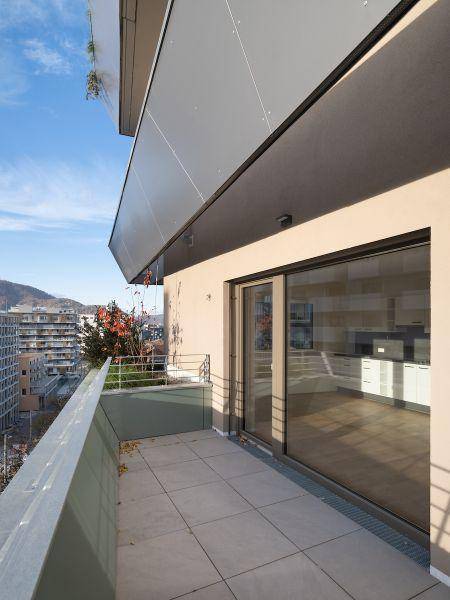 Geräumiger Balkon mit Fliesenboden und Schiebetür, bietet einen weiten Blick über die Stadt.