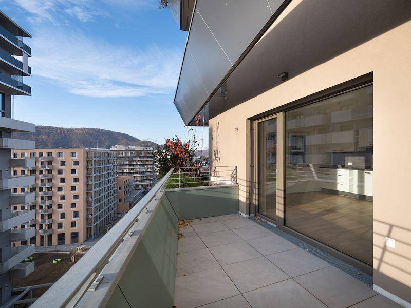 Großer Balkon mit Fliesenboden und Glasgeländer, bietet einen weiten Blick auf die Stadt und Hügel.