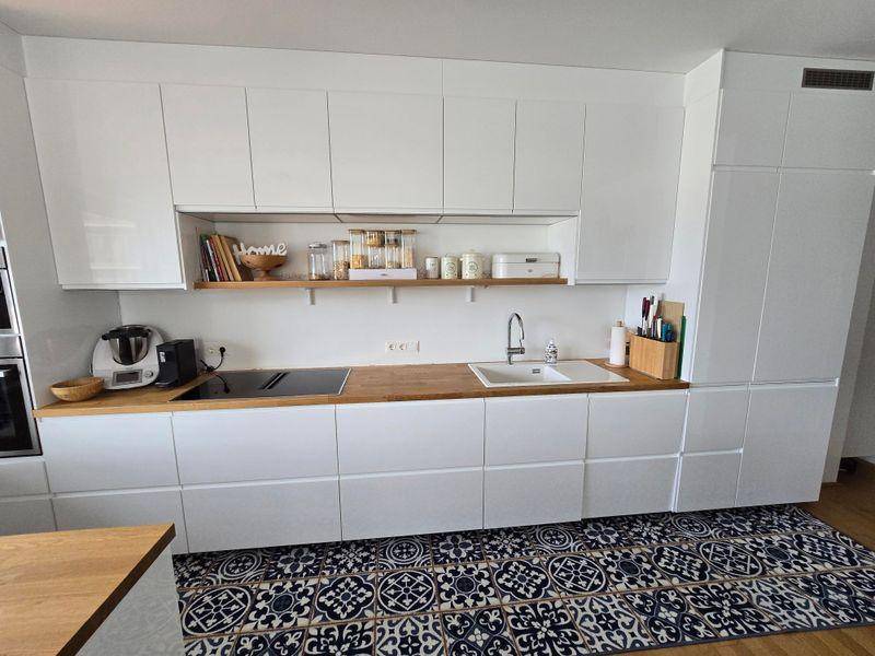 Helle Einbauküche mit weißen Schränken, Holzdetails und modernem Design.