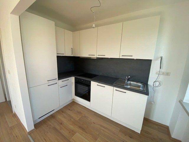 Kompakte, moderne Einbauküche mit weißen Schränken, dunkler Arbeitsplatte und integrierten Geräten.