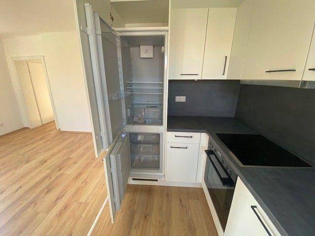 Integrierter Kühlschrank in der modernen Einbauküche mit weißer Front und dunkler Arbeitsplatte.