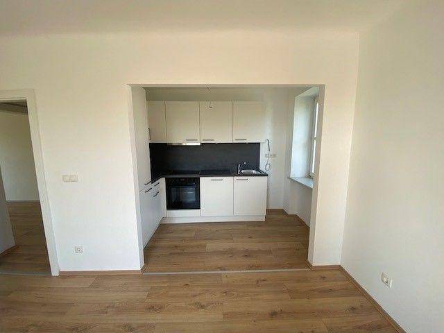 Helle, moderne Einbauküche in einer Nische mit Laminatboden und Blick in den angrenzenden Wohnbereich.