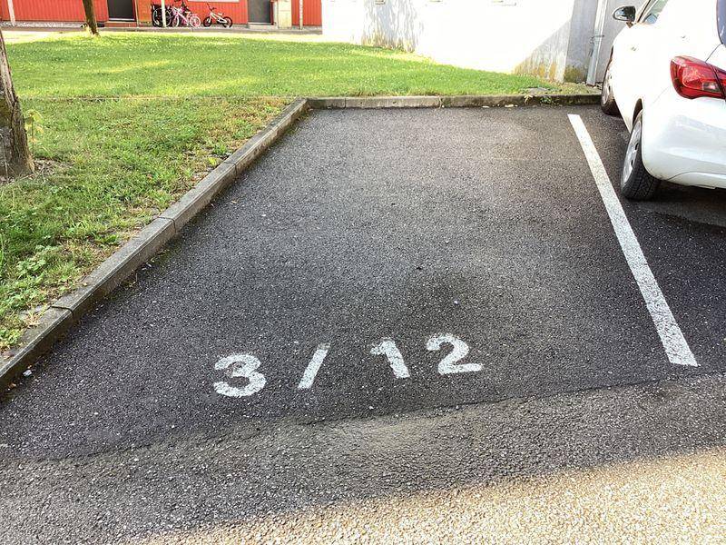Außenparkplatz mit Markierung für einen Stellplatz auf Asphaltboden neben einer Grünfläche.