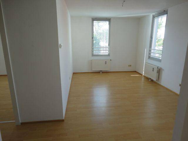 Geräumiger, heller Wohnbereich mit Laminatboden und zwei großen Fenstern, die den Raum erhellen.
