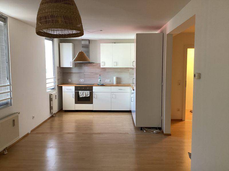 Offener Wohn- und Essbereich mit integrierter Küche, Laminatboden und großen Fenstern.