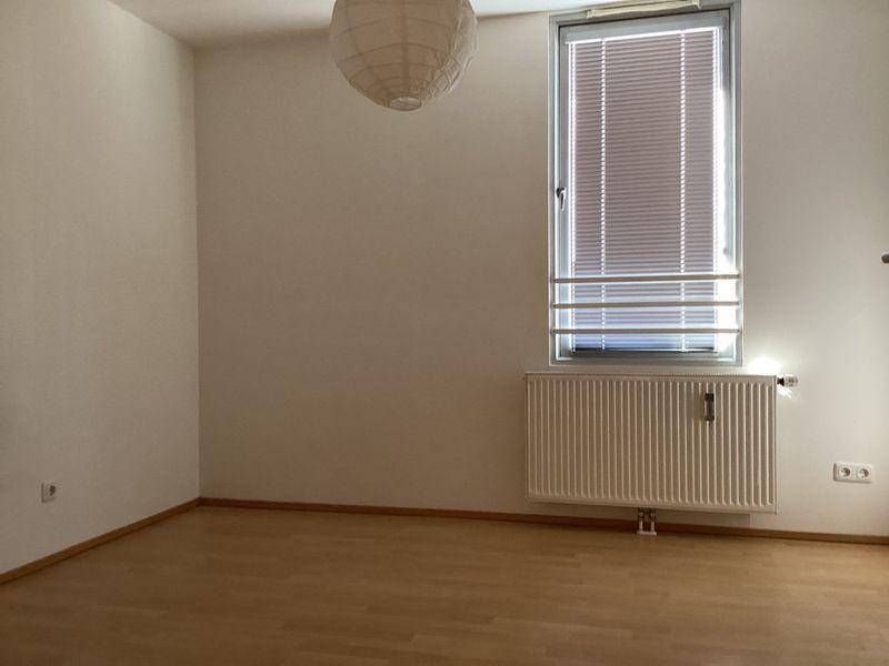Helles Schlafzimmer mit Laminatboden, einem Fenster mit Jalousien und einem Heizkörper.