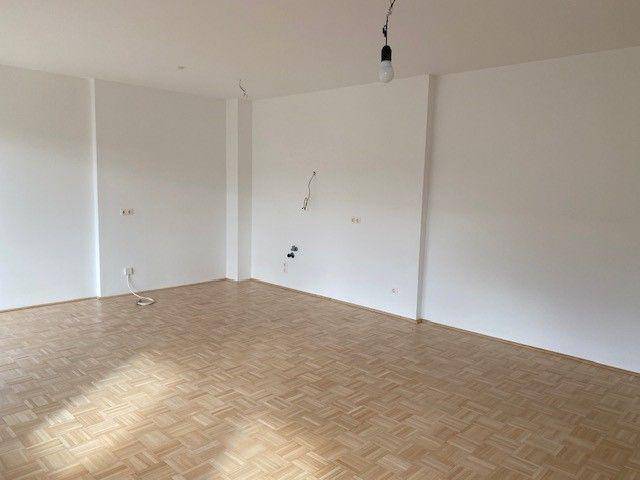 Großzügiger Wohnraum mit Parkettboden und weißen Wänden, ideal für moderne Wohnkonzepte.